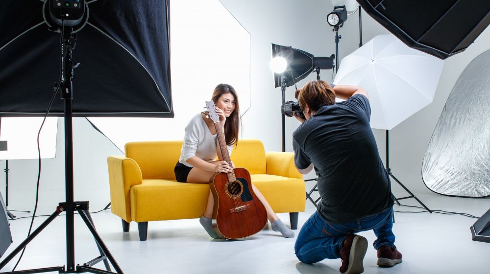 Junges Mädchen mit Gitarre auf einem gelben Sofa im Studio, nach professionellem Styling fotografiert