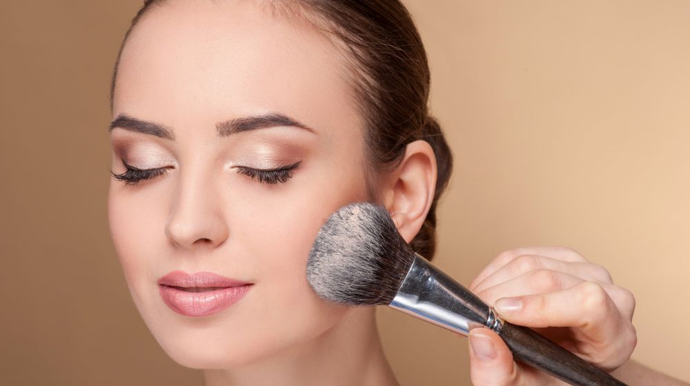 Frau wird von Maskenbildnerin mit Make-up-Pinsel für professionelles Styling geschminkt